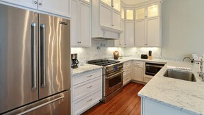 A modern kitchen with stainless steel appliances, white cabinetry, and a marble countertop. - Heated Pool Access | 5*Clean | Flex Cancelation (Savannah)