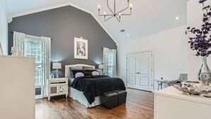 A bedroom with a large bed, a nightstand, a dresser, and a chandelier.