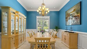 A dining room with a large wooden table, chairs, a chandelier, and a cabinet with glass doors.