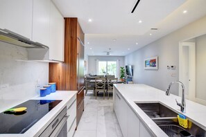 A modern kitchen with white cabinetry, a wooden accent wall, and a dining area with a table and chairs.