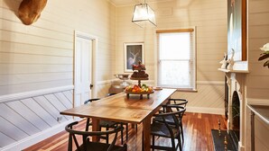 A dining room with a wooden table, black chairs, a deer head mounted on the wall, a chandelier, and a fireplace. - Inglenook Cottage Healesville (Healesville)