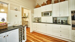 A kitchen with white cabinets, a microwave, and a wine rack. - Inglenook Cottage Healesville (Healesville)