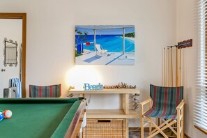 Ett biljardbord med bollar, en randig stol, en målning som föreställer en strandscen och en skylt med texten ”Beach”.
