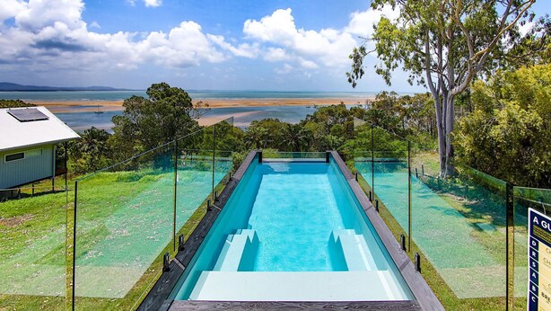 A rectangular pool with a glass barrier, surrounded by a grassy area and trees, overlooking a beach and ocean. - SPEEDYS SHACK   1770 - panoramic ocean & bay views (SEVENTEEN SEVENTY)