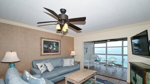 A living room with a blue sofa, a wooden coffee table, a ceiling fan, and a large window with a view of the ocean. - BEACHFRONT CONDO - THREE BEDROOM - HEATED POOL - FREE BOAT DOCKS - RENOVATED (Sarasota)