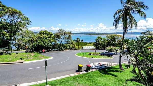 A coastal road with a stop sign, a roundabout, and a view of the sea and mountains.