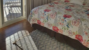 Une chambre à coucher comprenant un lit, un ventilateur de plafond, un tableau, une table de chevet et une vue sur l’océan par une porte coulissante.