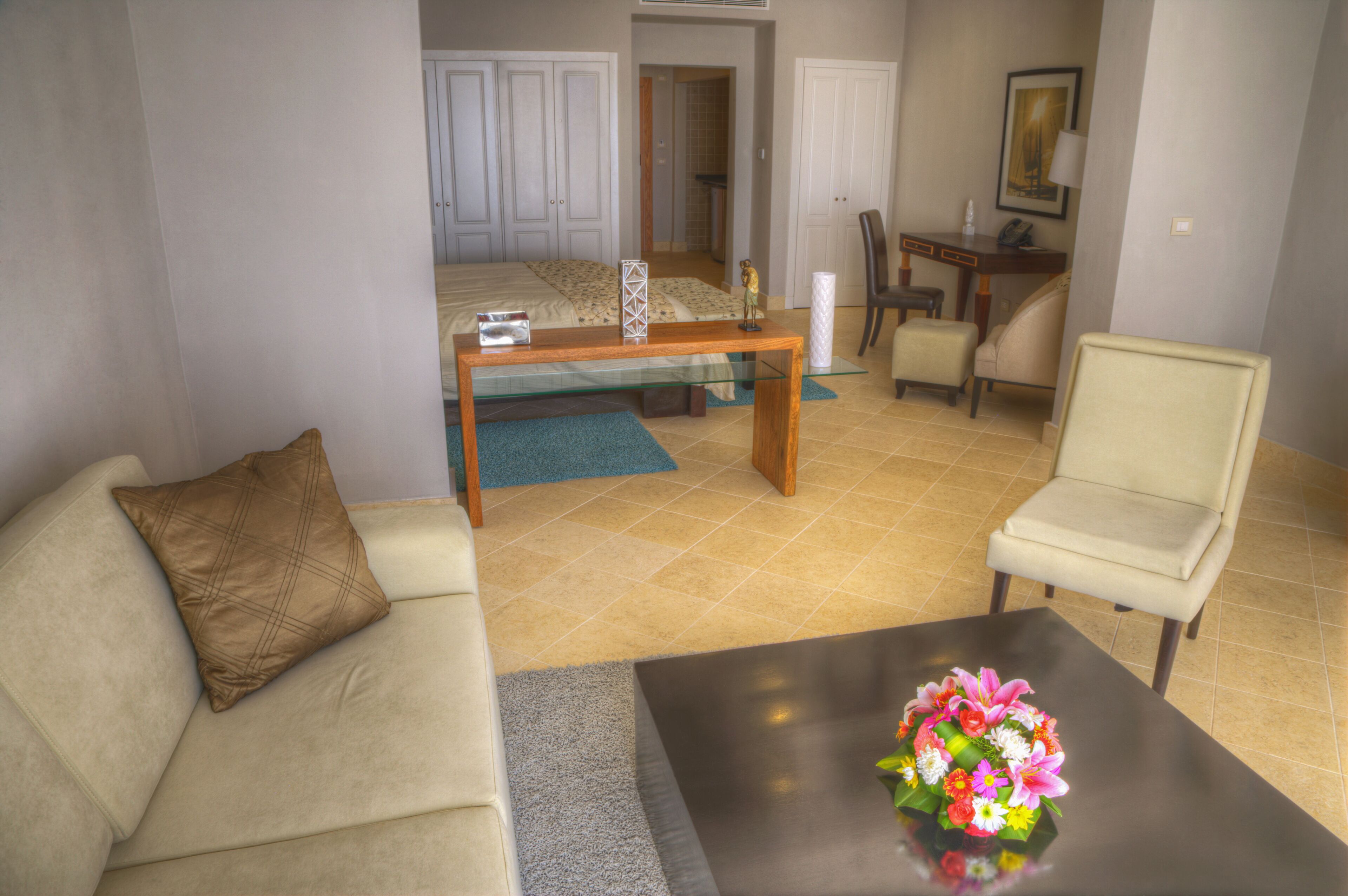 Een hotelkamer met een bed, een bureau, een stoel, een bank en een bijzettafeltje met bloemen.