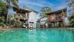 A pool area with two buildings, one with a balcony and the other with a wooden deck. - DAMIA VILLA 2 AGNES WATER (AGNES WATER)
