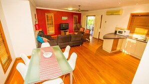 A compact living space with a dining area, a sofa set, a television, and a kitchen area with a microwave. - DAMIA VILLA 2 AGNES WATER (AGNES WATER)