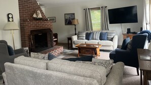 Una sala de estar con chimenea de ladrillo, un conjunto de sofás, un televisor y una lámpara.