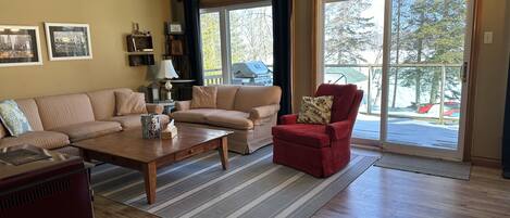Una sala de estar con sofá, sillón, mesa de centro y vistas al exterior a través de una puerta corrediza de vidrio.