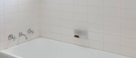 Un baño con una bañera blanca, una ventana con un cartel que dice 'BEACH' y una planta en maceta en el alféizar.