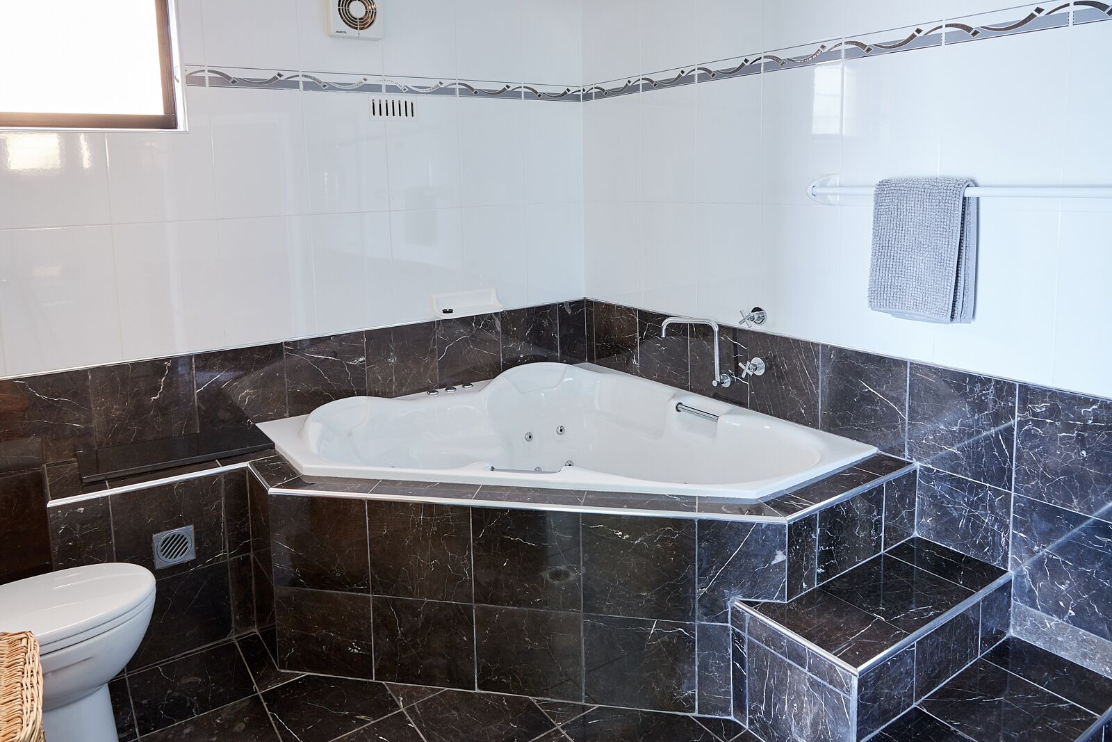 Un baño moderno con una bañera independiente, baldosas de mármol oscuro y un inodoro blanco.