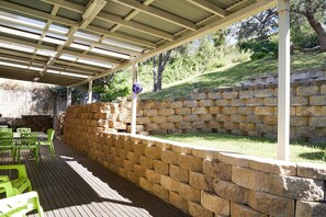 Un patio couvert avec un mur en pierre, des chaises vertes et une terrasse en bois.