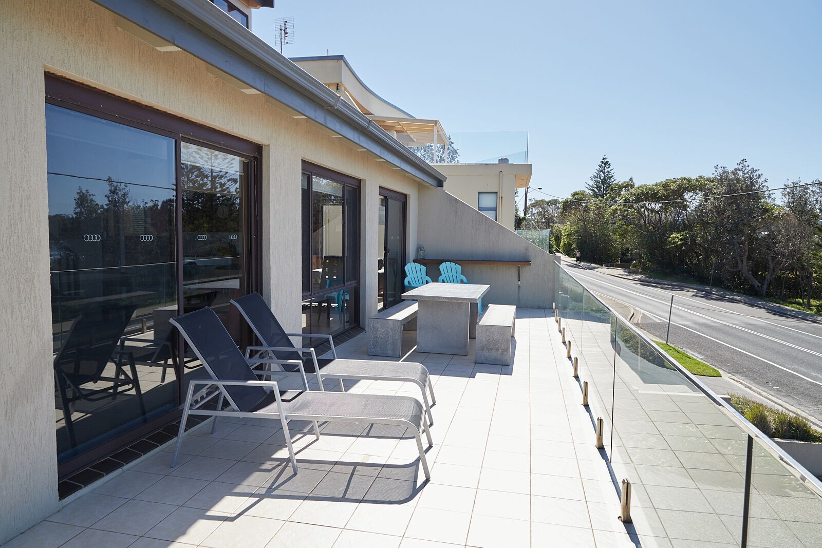A modern building with a patio area featuring outdoor seating and a glass railing overlooking a road.