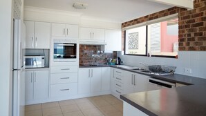 A modern kitchen with white cabinets, a microwave, and a brick accent wall. - A stone's throw from Mollymook Beach (Mollymook)