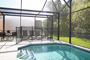 Una piscina scoperta coperta con una zona patio, sedie e un tavolo.