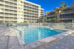 A swimming pool with a surrounding deck, lounge chairs, and a multi-story building in the background. - Doveplum 721- 2 bedroom 2.5 bath overlooking serene canal with private beach access (Siesta Key)