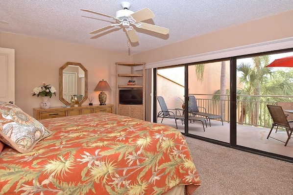 A bedroom with a bed, a ceiling fan, a large window, and a balcony with chairs. - Doveplum 721- 2 bedroom 2.5 bath overlooking serene canal with private beach access (Siesta Key)