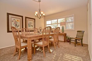 A dining area with a wooden table and chairs, a chandelier, framed artwork on the wall, and a window with blinds. - Doveplum 721- 2 bedroom 2.5 bath overlooking serene canal with private beach access (Siesta Key)