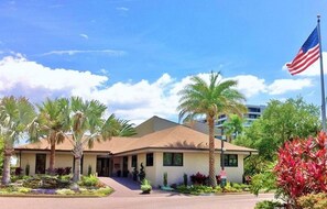 A hotel with a single-story structure, a flagpole with an American flag, and a well-maintained garden with palm trees. - Doveplum 721- 2 bedroom 2.5 bath overlooking serene canal with private beach access (Siesta Key)