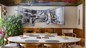 Uma sala de jantar com uma mesa redonda, cadeiras de madeira e um quadro grande na parede.