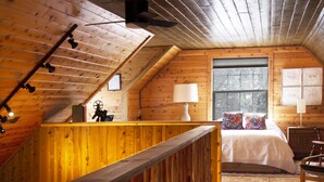 Uma cabana de madeira com quarto no mezanino, escada de madeira e vista para o exterior.