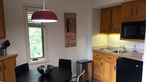 Cozinha compacta com armários de madeira, geladeira preta, micro-ondas e área de jantar com mesa e cadeiras pretas.