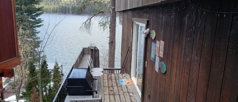 A wooden deck with a grill and chairs overlooking a lake.