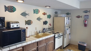 A kitchen with a microwave, toaster, stove, and refrigerator. There are decorative fish on the wall and a trash can.