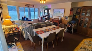 A cozy living room with a sofa, a dining table, and a bar area with arcade games.