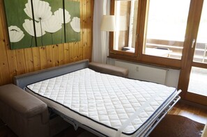 Una habitación con cama, banca, cuadro, ventana y lámpara.