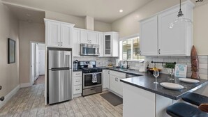 A modern kitchen with white cabinets, stainless steel appliances, a marble countertop, and a bar area with stools. - Vintage Flat | Mins to Golden 1 Center, Capitol (Sacramento)