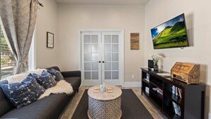 A living room with a sofa, a coffee table, a bookshelf, a television, and a door with frosted glass panels. - Vintage Flat | Mins to Golden 1 Center, Capitol (Sacramento)