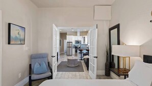 A hotel room with a bed, a chair, a desk, a lamp, a painting, and a view into the kitchen area. - Vintage Flat | Mins to Golden 1 Center, Capitol (Sacramento)
