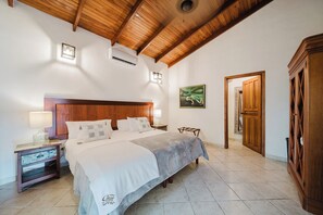 A bedroom with a wooden ceiling, a bed with a white bedspread, a nightstand with a lamp, and a wooden wardrobe. - Private piece of luxury living in Manuel Antonio - 5 minutes to Marina Pez Vela. (Manuel Antonio)