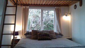 Ett sovrum med en våningssäng, en stege, ett sängbord med en lampa och ett fönster med gardiner.