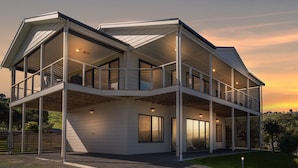 Une maison moderne à deux étages, dotée d’un balcon au premier étage et d’une terrasse couverte au deuxième.