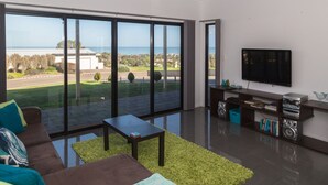 Un salon moderne doté d’une grande porte-fenêtre coulissante donnant sur un balcon avec vue sur la mer.