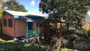 A small wooden cabin with a porch, surrounded by lush greenery and a clear blue sky. - Cottage with sea view (Gros Islet)