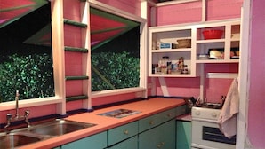 A kitchen with teal cabinets, a pink countertop, and a window with a view of greenery. - Cottage with sea view (Gros Islet)
