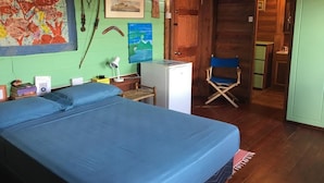 A room with a bed, a desk, a chair, a small refrigerator, and a door leading to another room. - Cottage with sea view (Gros Islet)