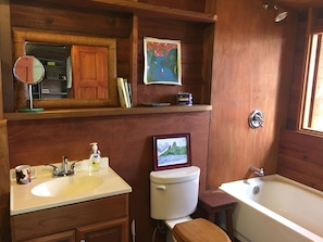 A bathroom with a wooden vanity, a toilet, a bathtub, a mirror, and a framed picture on the wall.