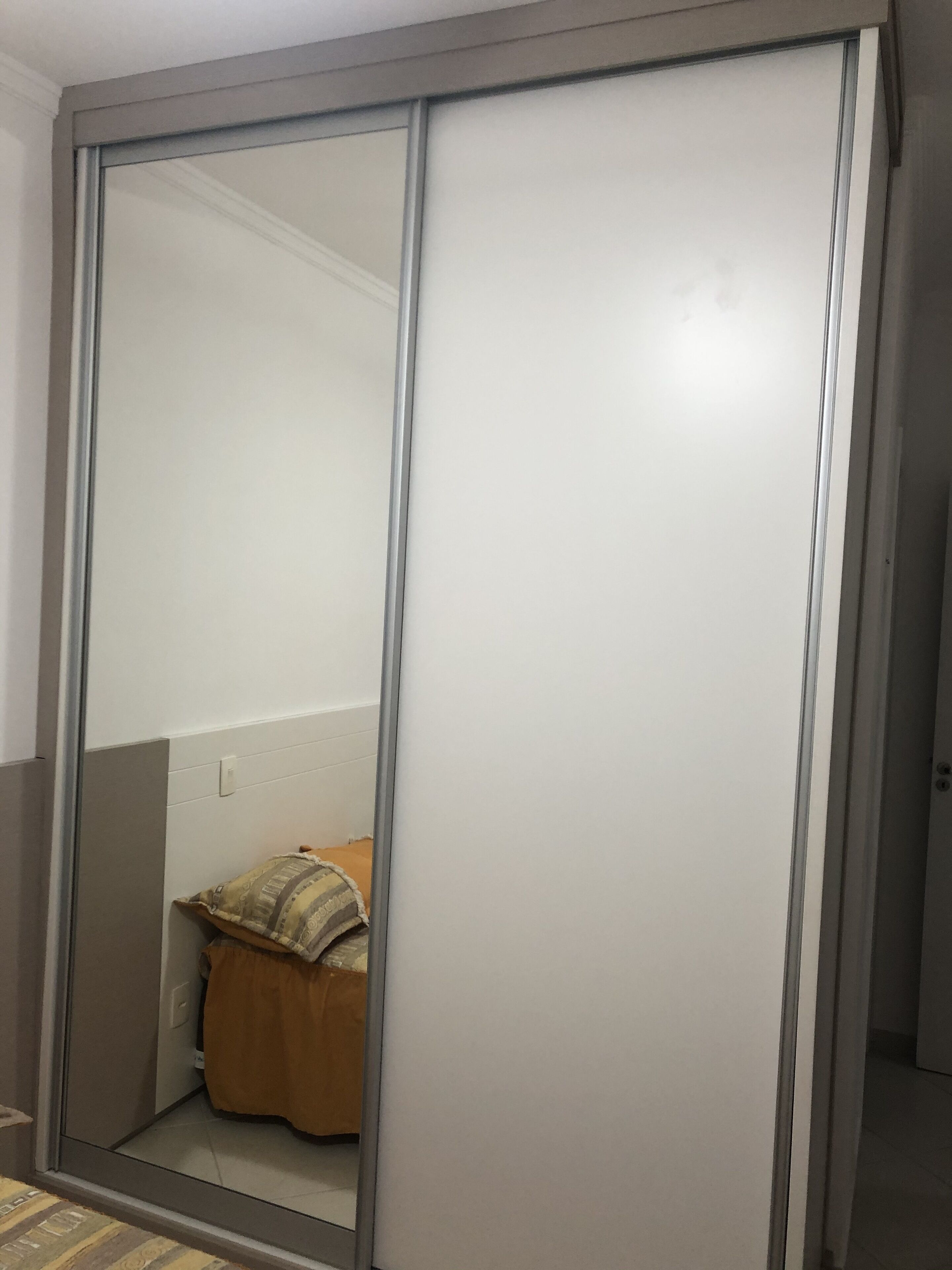 Ein Zimmer mit Schiebetürenschrank, einem Bett mit brauner Bettdecke und einem Kissen mit Muster.