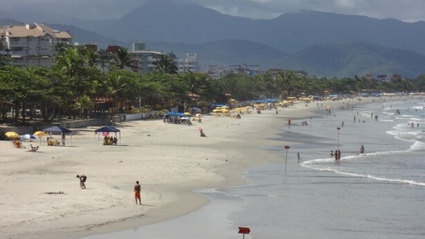 Une plage avec des parasols, des gens et des bâtiments en arrière-plan.