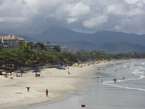 A beach with umbrellas, people, and buildings in the background.