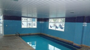 Une piscine intérieure aux murs recouverts de carreaux bleus, offrant une vue dégagée sur l’extérieur grâce à de grandes fenêtres.