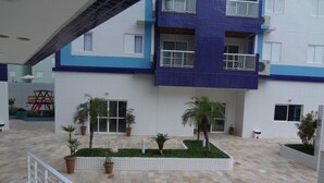 Un immeuble à plusieurs étages, doté d’une façade recouverte de carreaux, d’une cour intérieure agrémentée de plantes en pot et d’une balustrade blanche.