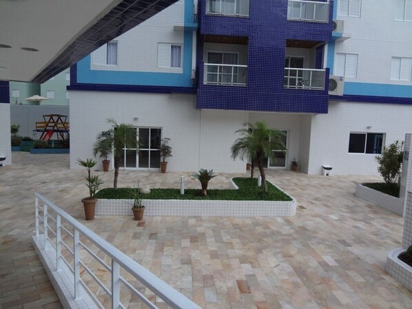 A multi-story building with a tiled exterior, a central courtyard with potted plants, and a white railing.